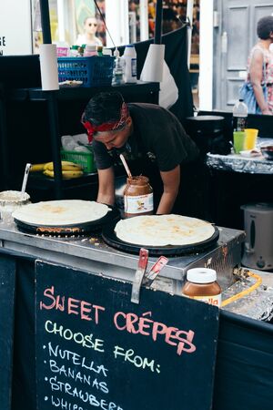London/UK - July 20 2018: woman making savoury crepes with hazelnut cocoa spread and bananas on Portobello market, London, UKのeditorial素材