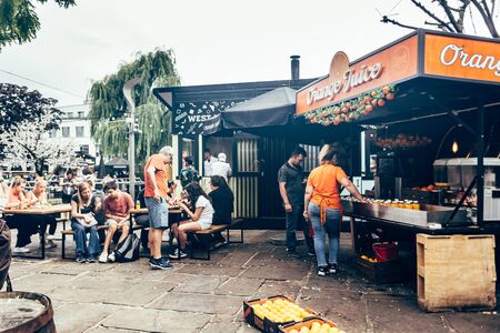 London/UK - July 17, 2019: people resting at Camden Market sitting area; Orange Juice market stall...