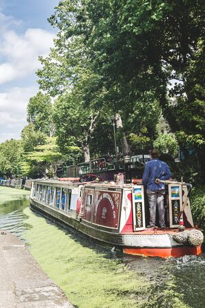 London/UK - 17/07/2019: man on a stern controlling the navigation of a waterbus in Regents Canal in London. A boat service shuttling between Camden Lock and Paddington Arm of the Grand Union Canalのeditorial素材