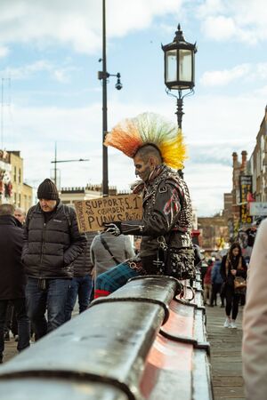 London / UK - Dec 01, 2019: tattoed face punk with colorful mohawk sitting on the street in Camden Town. The punk subculture emerged in the United Kingdom and the United States in the mid-1970sのeditorial素材