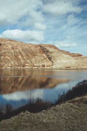 A motorboat sailing on a lake in Scotland; surrounding hills and the blue sky reflects in the water surfaceの写真素材