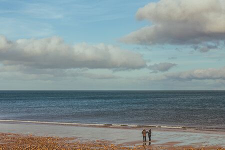 A couple walking on the beach in spring at the North Sea side in Brora village in Scotland, UKの写真素材