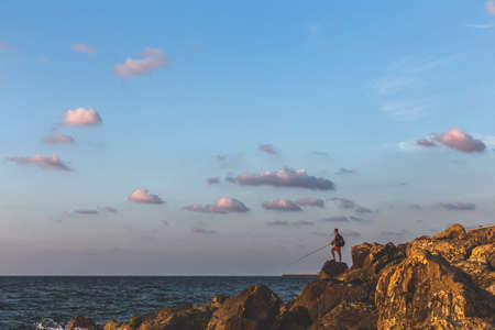 Tel Aviv/Israel-10/10/18: man fishing with a fishing rod on the breakwater near Tel Aviv Marina on the sunsetのeditorial素材