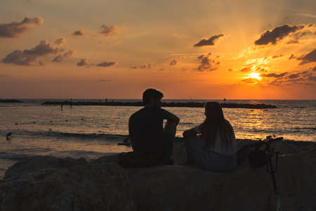Tel Aviv/Israel-8/10/18: Silhouettes of a young couple sitting on the Mediterranean shoreline in Tel...