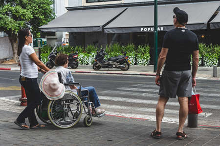 Tel Aviv/Israel-9/10/18: a personal care attendant with a disabled woman in a wheelchair waiting for a green signal on a crosswalk in Tel Aviv, Israelのeditorial素材