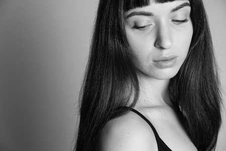 Close up studio portrait of a pretty brunette woman in a black spaghetti strap top, looking at her shoulder, half-turned, against a plain grey backgroundの写真素材