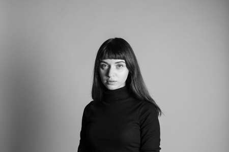 Studio portrait of a pretty brunette woman, wearing folded black polo-neck sweater, looking at...