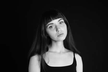 Studio portrait of a pretty brunette woman in a black spaghetti strap top, looking at the camera,...