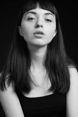 Close up studio portrait of a pretty brunette woman in a black spaghetti strap top, looking at the...