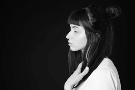 Sideview studio portrait of a pretty brunette woman in a white blank t-shirt, against a plain black background, looking to the sideの写真素材