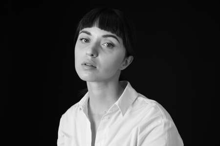 Studio portrait of a pretty brunette woman in a white shirt, against a plain black background,...
