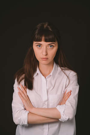 Studio portrait of a pretty brunette woman in a white shirt against a plain black background, looking at cameraの写真素材