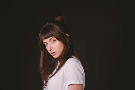 Studio portrait of a pretty brunette woman in a white blank t-shirt, against a plain black...