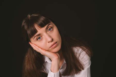 Studio portrait of a pretty brunette woman in a white shirt, against a plain black background, seriously looking at the cameraの写真素材