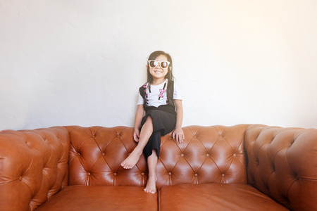 Asian girl with sunglasses sitting on a leather sofa in the holiday mood.の写真素材