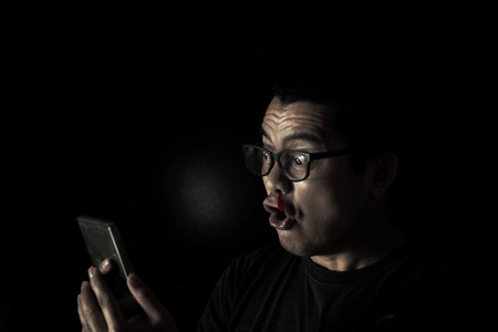 Asian men in the dark facial expression lust while browsing smartphonesの写真素材