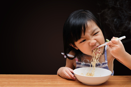 Asian child girl eating Instant noodles isolated on black background, with clipping pathの写真素材