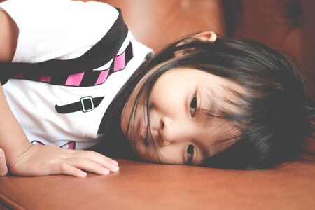 Asian child girl in a sad mood lonely lying on the couchの写真素材