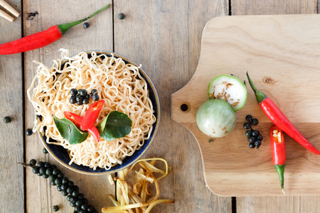 Instant noodles in a bowl with chili pepper and lime leaves on old wooden table