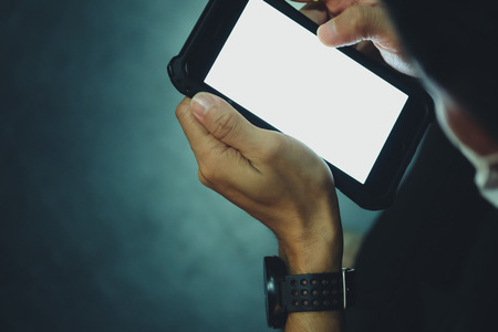 Close up of hand of man using mobile smart phones in the dark, empty space white screen on smart phone for text or Logoの写真素材