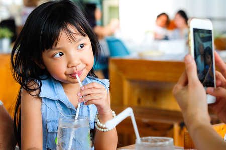 Asian child girl drinking water and poses taking pictures from mobileの写真素材