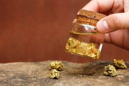Human hands are holding bottles that contain pure gold minerals found in mines on black backgroundの写真素材