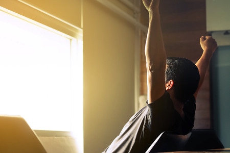 Asian men are holding their arms and fists to loosen their gaze out of the morning window, ready for the first day's work.の写真素材