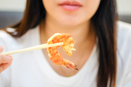 Asian women are using chopsticks to pick up shrimp with selective focusの写真素材