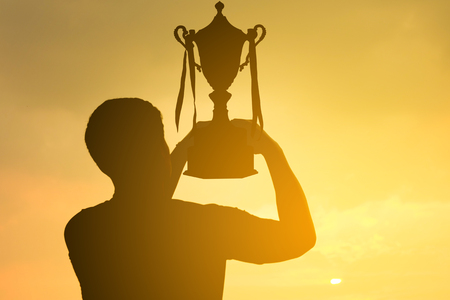 silhouette of a man holding up trophy on sunset skyの写真素材