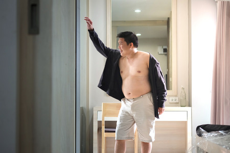 Fat Asian man are standing off the shirt. Due to hot weatherの写真素材