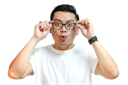 Young asian man wearing white t-shirt and glasses facial expression surprised on white backgroundの写真素材
