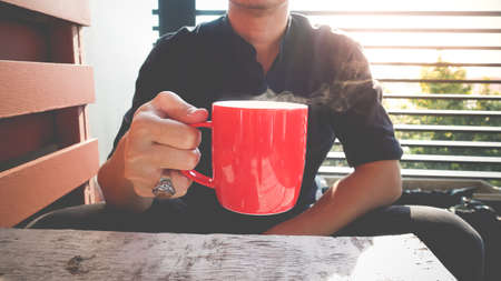 Hand of man holdinging coffee or tea with hot steam in the morning in red glassの写真素材