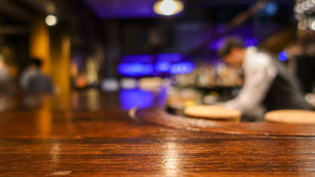 Wooden bar table in front of abstract blurred background of restaurant in the darkの写真素材