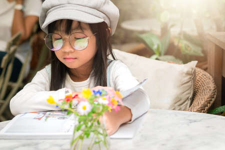 An Asian girl wearing glasses and a hat is sitting reading a book. On the marble table in her houseの写真素材