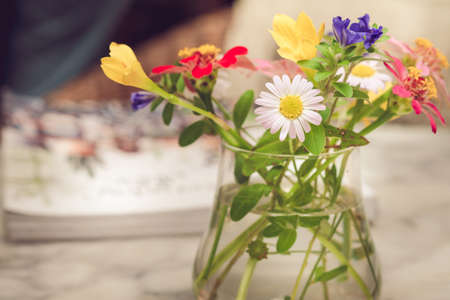 Colorful cute flowers in a clear glass vase placed on the tableの写真素材