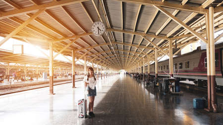 Asian woman tourist with a suitcase is standing waiting for the train at the train station during...