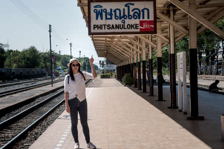 Phitsanulok Thailand - October 28, 2019: Asian tourist with a gray backpack is standing pointing at the Phitsanulok train station signのeditorial素材