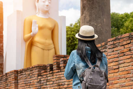The back of an Asian woman wearing a hat and denim shirt paying respect  Buddha statues