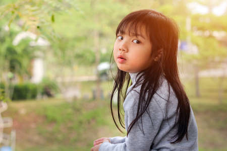 Asian child girl looking back on the side on green outdoor backgroundの写真素材