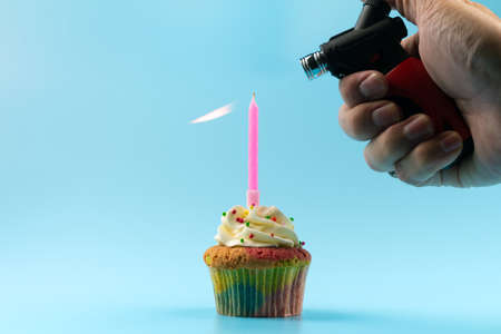 A man's hand is lighting a candle on a cupcake on a blue background.の写真素材