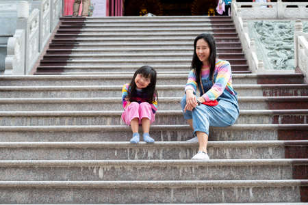 Asian mother and daughter are wearing jeans, T-shirts of many colors, smiling mood and sitting happily photographed with love in temples, the concept of family lifestyle.の写真素材