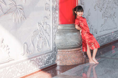 Asian child girl smiling in red dress standing on cement wall background, Concept costume Chinese new yearの写真素材