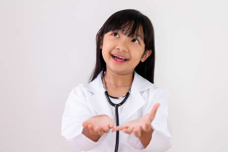 Asian child girl dressed in a doctor's uniform is carrying both hands with a smiling face on a white background.の写真素材