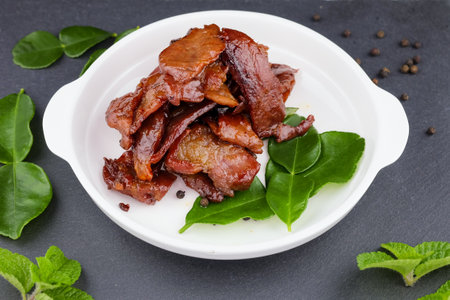 Deep fried sun dried pork in white dish with kaffir lime leaves and pepper seeds on slate plateの写真素材