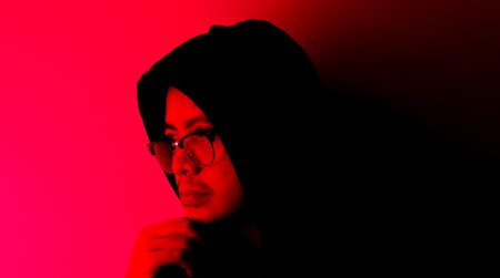 An Asian man in a black robe was wondering or thinking about something in the dark with red lights.の写真素材