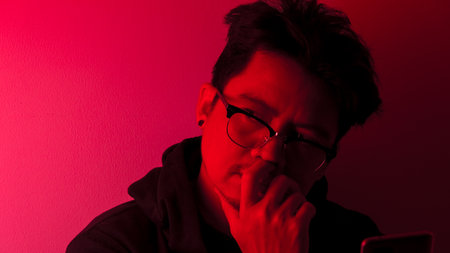 An Asian man in a black robe was wondering or thinking about something in the dark with red lights.の写真素材