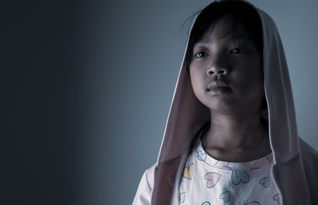 young Asian child girl wearing a robe has a sad face lonely in the dark.の写真素材