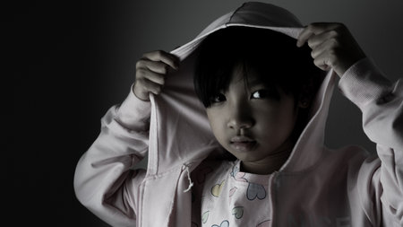 young Asian child girl wearing a robe has a sad face lonely in the dark.の写真素材