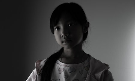 young Asian child girl wearing a robe has a sad face lonely in the dark.の写真素材