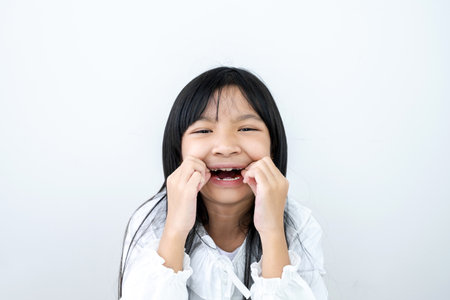 Asian child girl in a white shirt and teeth with braces on a white backgroundの写真素材